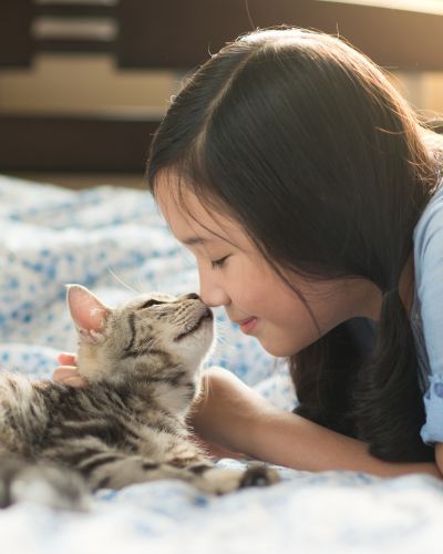 A girl and a cat are nose to nose laying down.